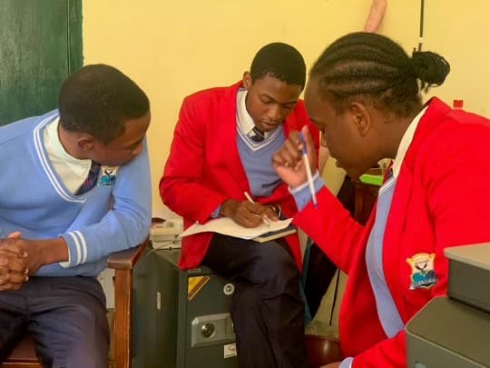 Three students in school uniforms collaborating over a notebook, peer guidance and shared learning